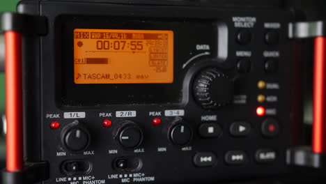 a man pressing the record button on an audio field recorder in a video production studio with volume displayed on a digital level display