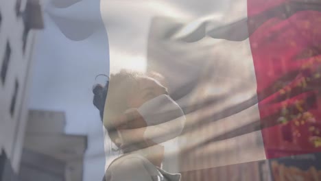 Animation-of-flag-of-france-waving-over-african-american-woman-wearing-face-mask-in-city-street