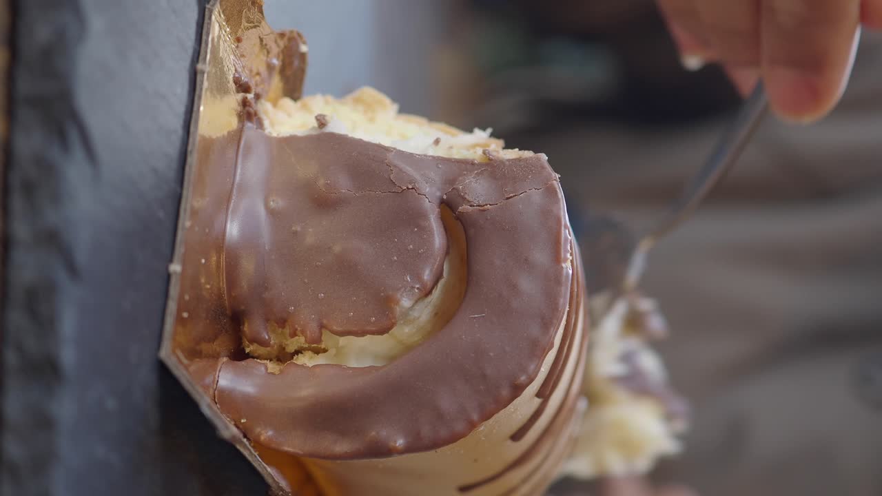 Close-up de uma mão comendo uma sobremesa coberta de chocolate com um garfo