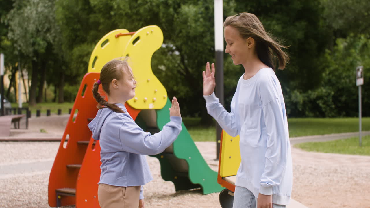 una niña con síndrome de down dando cinco y abrazando a otra niña en el parque en un día ventoso