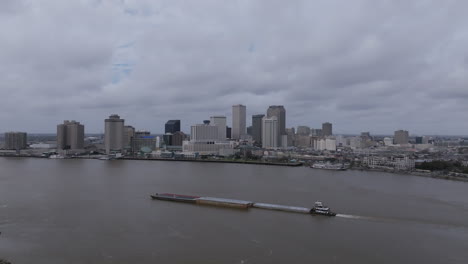 Imágenes-Aéreas-Volando-Hacia-Atrás-Lejos-De-Una-Gran-Barcaza-Que-Navega-Por-El-Río-Mississippi-Con-El-Centro-De-Nueva-Orleans-Al-Fondo