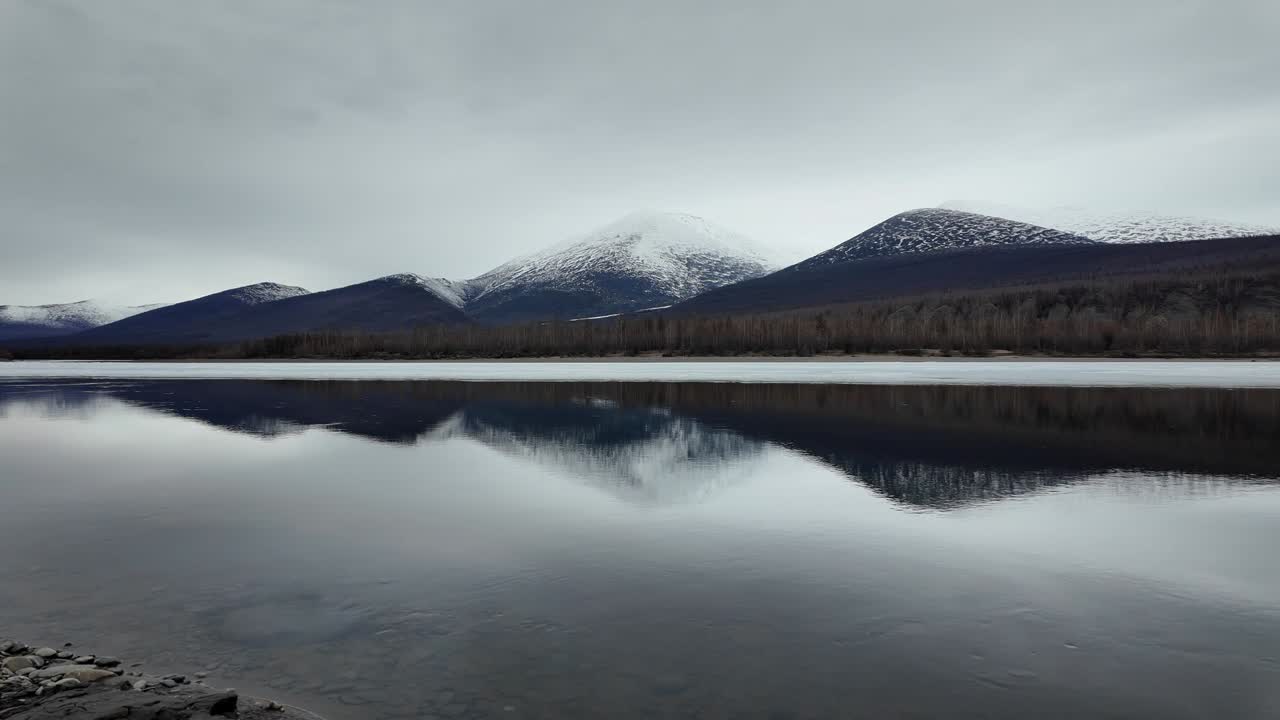 flujo lento de otra mitad del río congelado contra el fondo de un cielo gris y montañas nevadas 4k