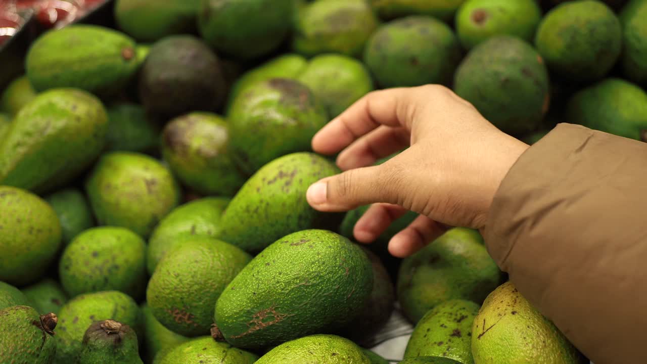 persona seleccionando aguacates en una tienda de comestibles