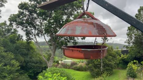 Beautiful-tranquil-slider-shot-of-an-antique-old-bird-table-suspended-in-the-foreground-in-fron-of-a-lush-and-serene-Queenland-hinterland-valley