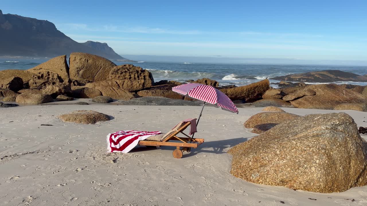 En rød og hvit parasoll og en strandstol på en strand.