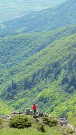 Aerial vertical view of a girl hiking across rocky mountain paths in the Balkans. Filmed in spring under a bright blue sky with beautiful panoramic views.