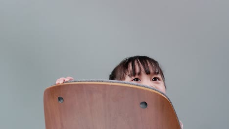 girl playing to hide behind wooden armchair