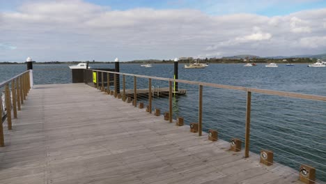 empty wooden boardwalk and jetty with a view of yachts and boats anchored on the calm sea from the strand in tauranga, new zealand