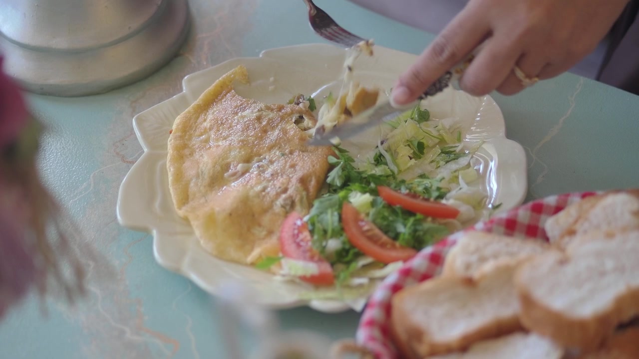 Close-up de Mãos Cortando Omelete e Salada à Mesa