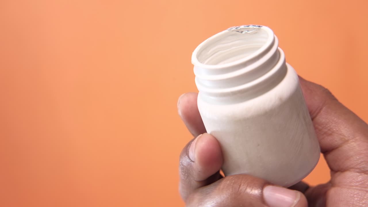 mano con un frasco de plástico blanco