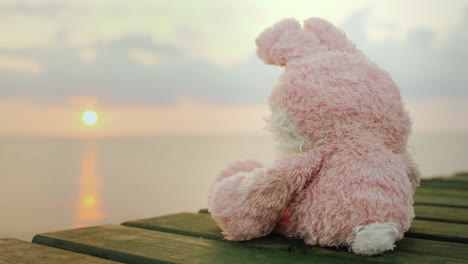 pink toy hare sitting on the pier looking at the rising sun 4k video