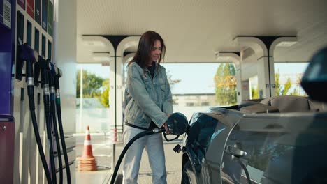 portrait of a happy brunette girl who refuels her dark gray convertible. refuel your car with joy