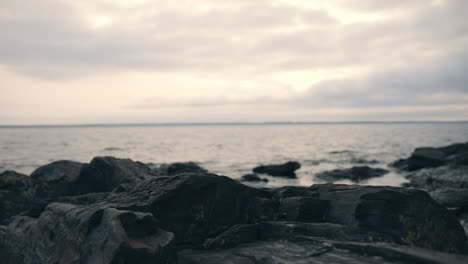 Handheld-low-angle-view-of-small-waves-hitting-cliffs,-on-a-rocky-shore,-on-a-moody,-cloudy-autumn-day,-in-Finland