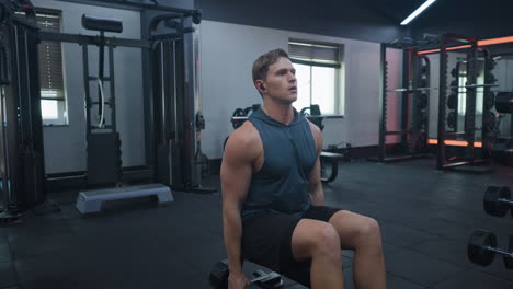 athletic blond male doing shoulder side lateral raise exercise with dumbbells in gym