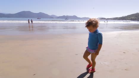 camera orbiting around young cute girl walking on the beach with mountains background and calm sea