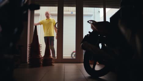 inside view guy in yellow t-shirt closes garage with motorcycle. end of the working day at the motorcycle school