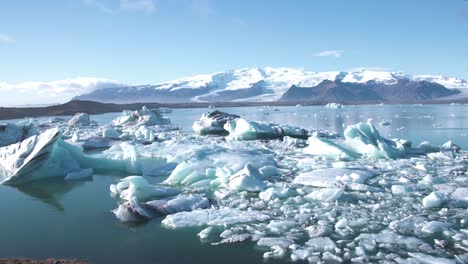 Meereslagune-In-Island-Mit-Eisschollen,-Schneebedeckte-Berge-Am-Horizont