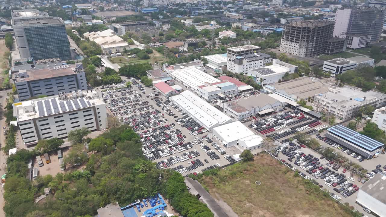 A scenic drone shot of Mogappair area near a car factory that is filled with car parked outside in hot sun