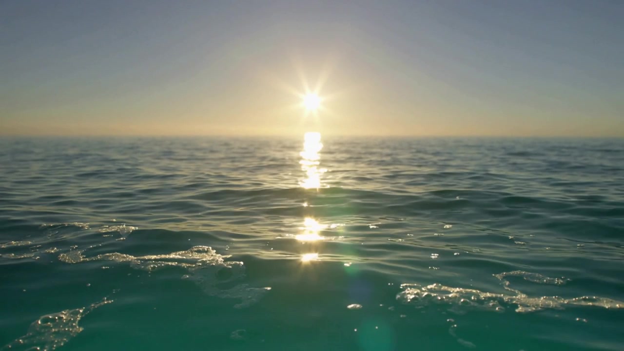 Gyngende kamera fanger solen og skiftende refleksion med dønninger over åbent hav, grøn linseflare