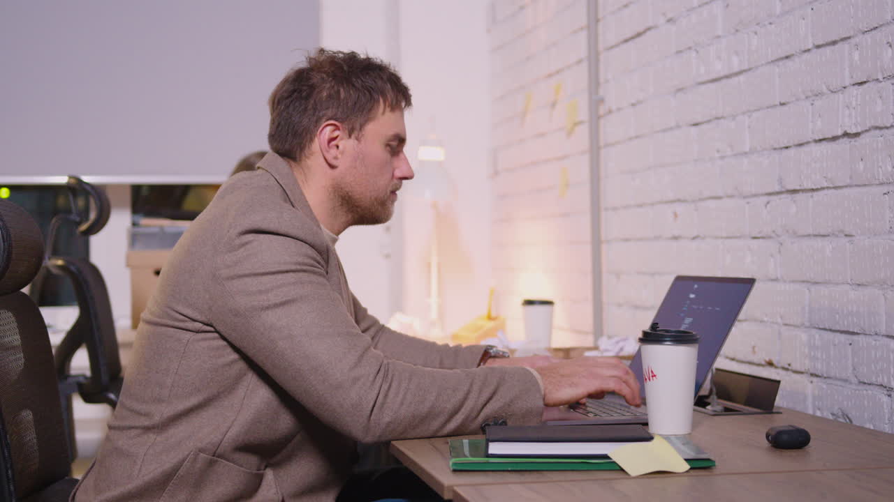 Businessman Typing On Laptop Computer And Drinking Takeaway Coffee In A Coworking Office