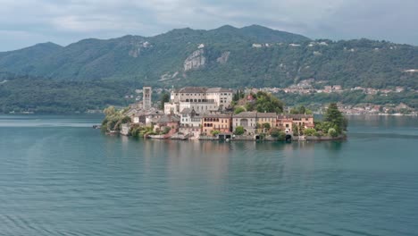 이탈리아 오르타 호수에 있는 산 줄리오 섬 (isola di san giulio) 은 물과 푸른 언덕에 둘러싸인 역사적인 건물과 함께 배경으로 공중에서 볼 수 있습니다.