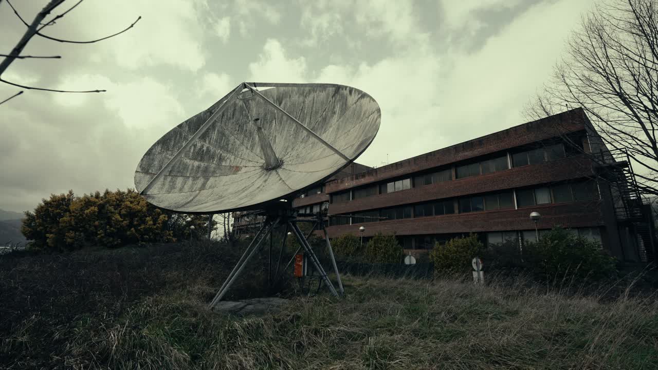 Övergiven parabolantenn och gammal byggnad under en molnig himmel