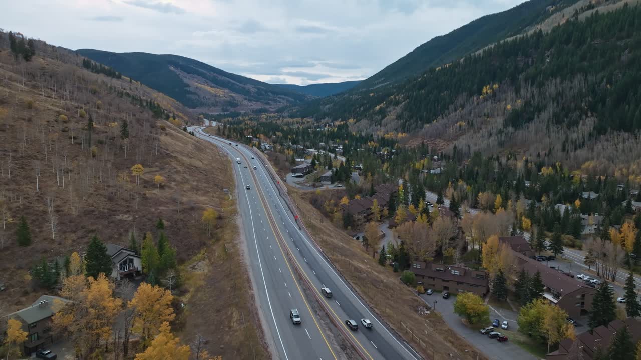 Highway roads along mountain slopes, showcasing autumn colors in full display under overcast shadowy sky in the valley, Vail Colorado