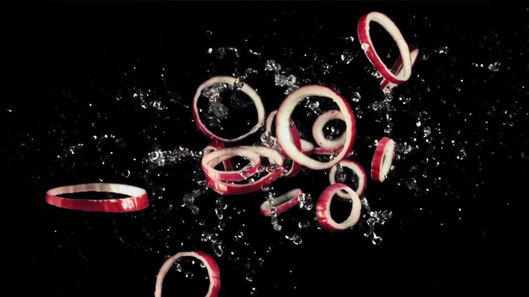 Anelli di cipolla rossa che schizzano nell'acqua su sfondo nero.