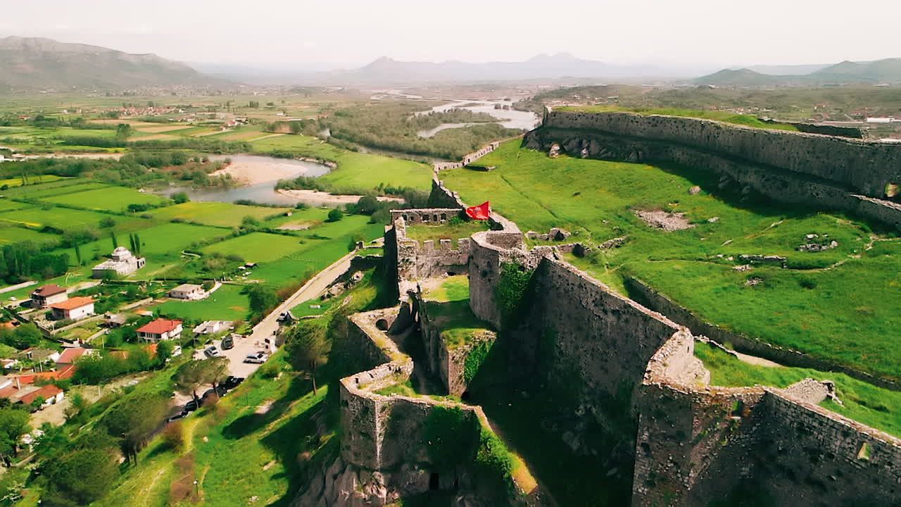 vista aérea volando lejos de la bandera albanesa en las ruinas del castillo en una colina