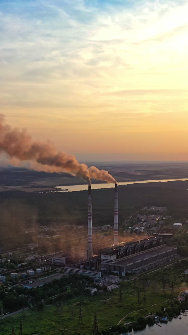 Smoke from pipes on factory near the river at sunset. Air pollution from industrial plant on the natural background in the evening. Vertical video