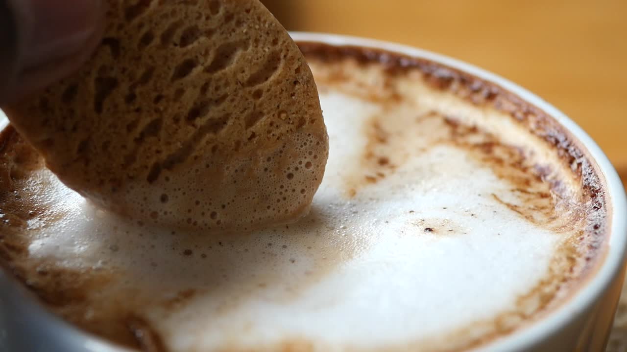 Hand holding cookie over cappuccino