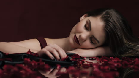 Porträt-Einer-Schönen-Kaukasischen-Frau,-Die-Mit-Fallenden-Rosenblättern-Spielt,-Sinnliche-Frau,-Die-Von-Intimer-Fantasieromantik-Träumt-Und-Dem-Verlangen-In-Rotem-Hintergrund-Valentinstagskonzept-Frönt