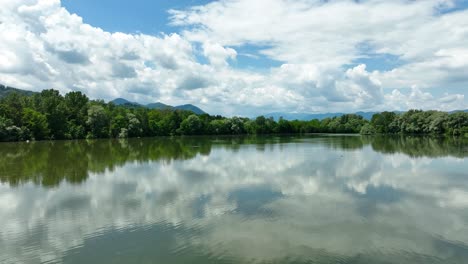 aerial above lake žovnek slow motion water reflection landscape, green forest and blue skyline, drone shot in slovenia, braslovče