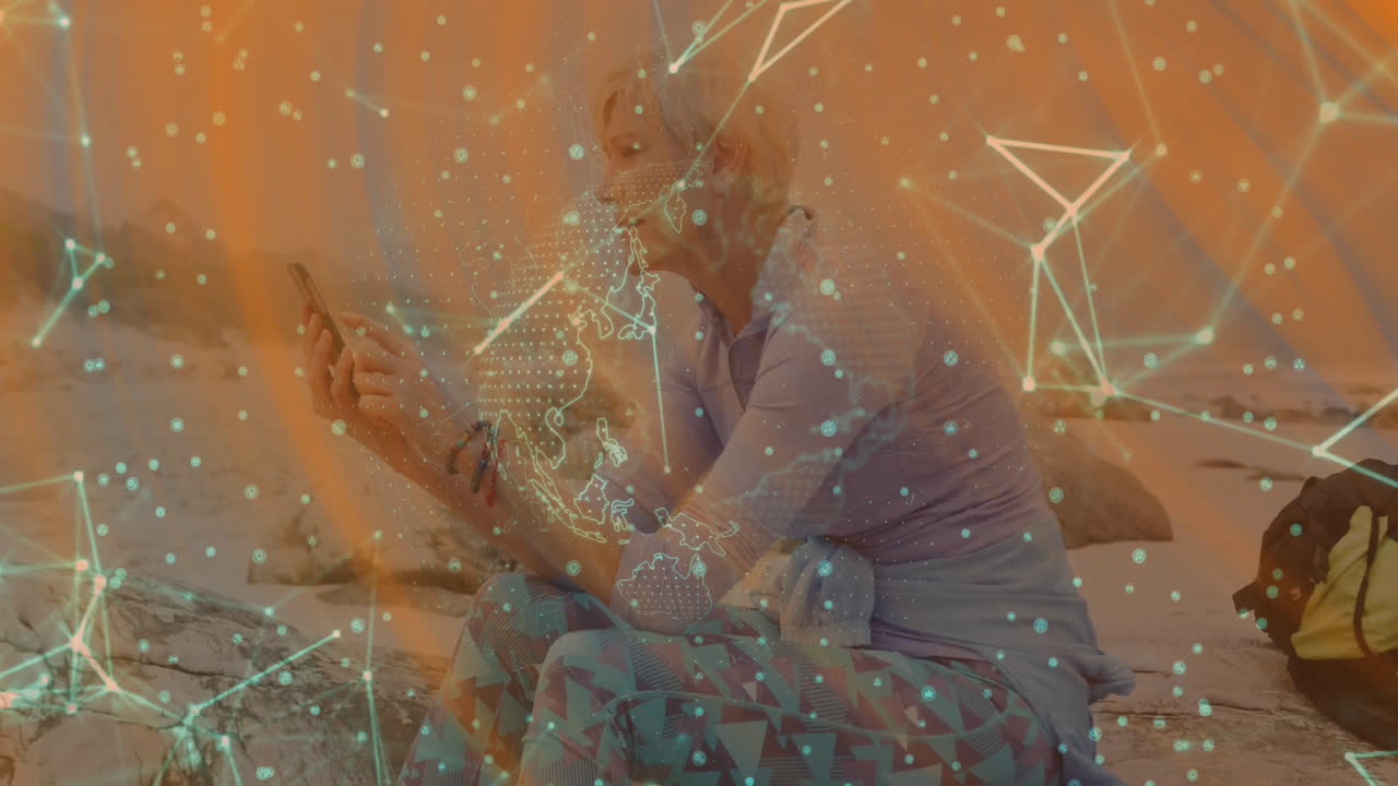 Woman using smartphone sitting on coastal beach rock, projecting digital technology network overlay