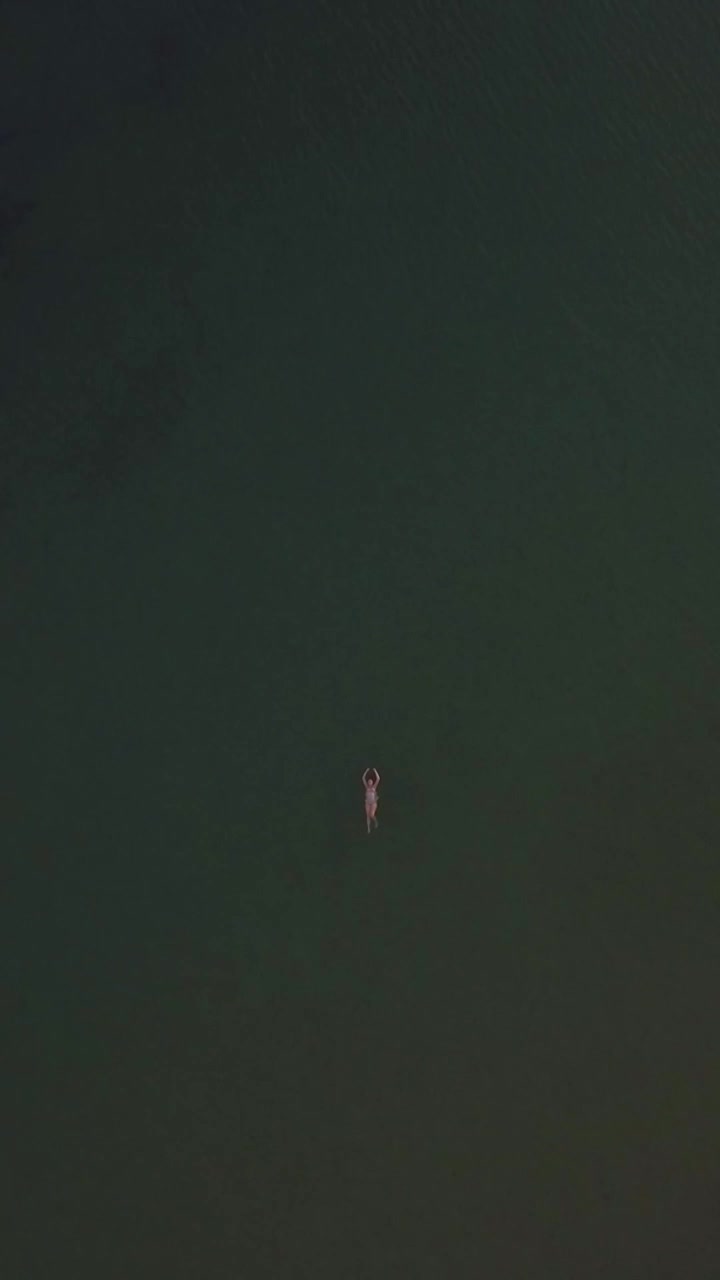 Aerial shot of woman swimming in the sea. Distant view