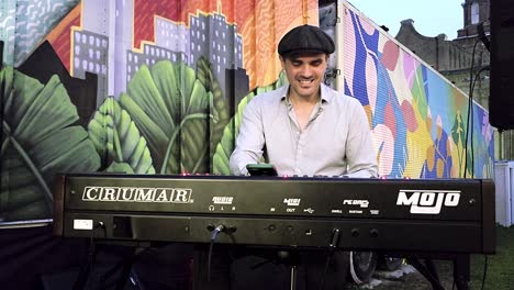 man playing keyboard at outdoor concert with graffiti mural in background
