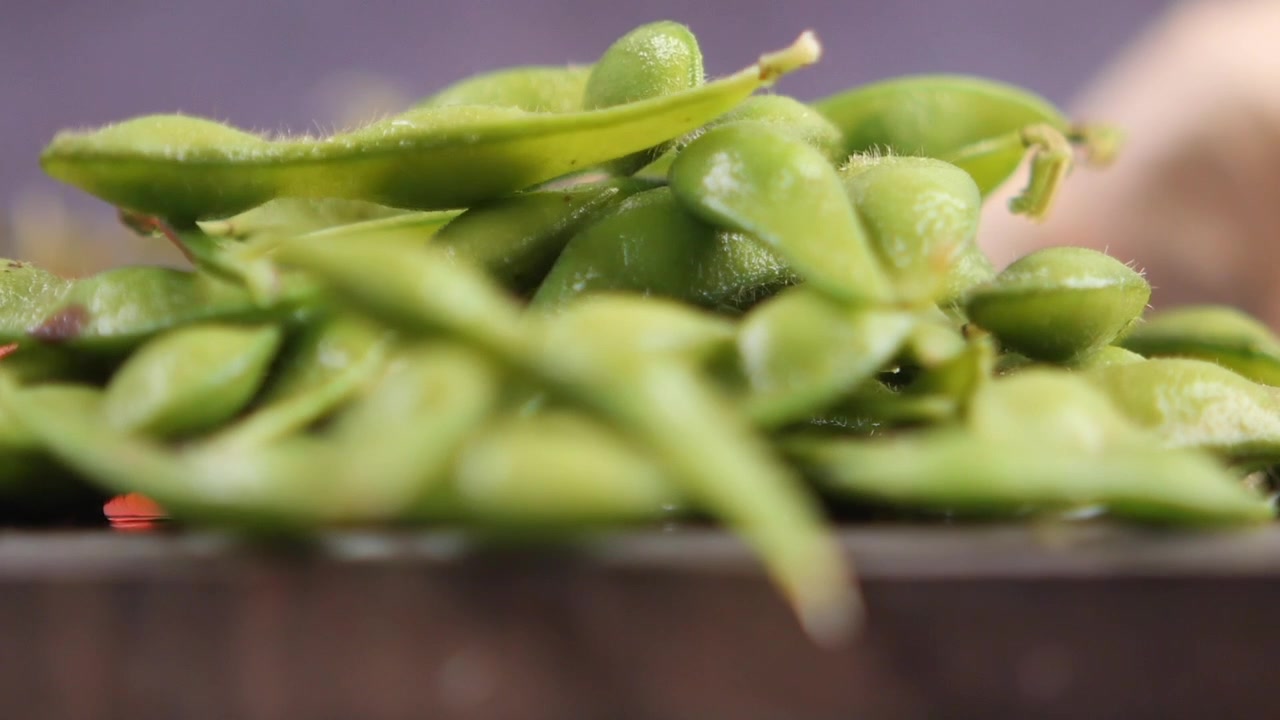 Fresh Edamame Beans Falling onto a Wooden Cutting Board