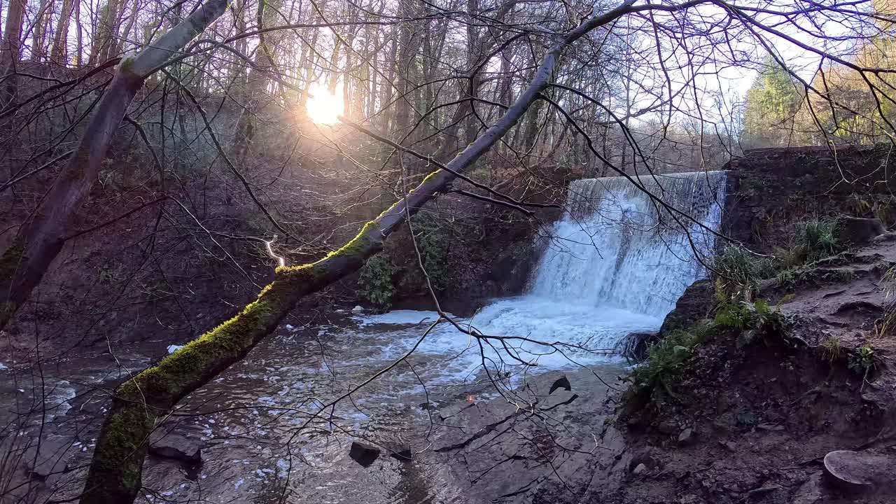 Solen står op over et vandfald, der kaskaderer i slow motion over en efterårsskovbæk.