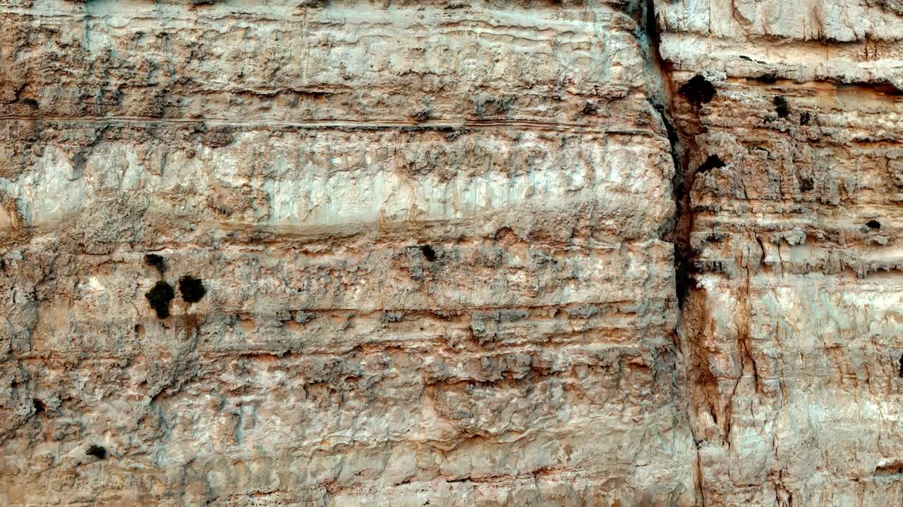 Nært billede i øjenhøjde af en robust kalkstensklippe med dramatiske, vandrette sedimentlag og lodrette revner under en strålende sommersol, der viser naturlige jordfarver i beige, tan og varm okker