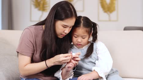 A mother applies a band-aid to her child's finger in a cozy living room setting, conveying care and tenderness