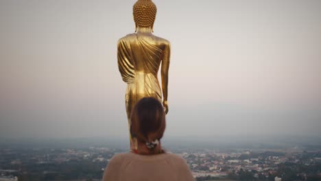 woman walks close to golden buddha statue