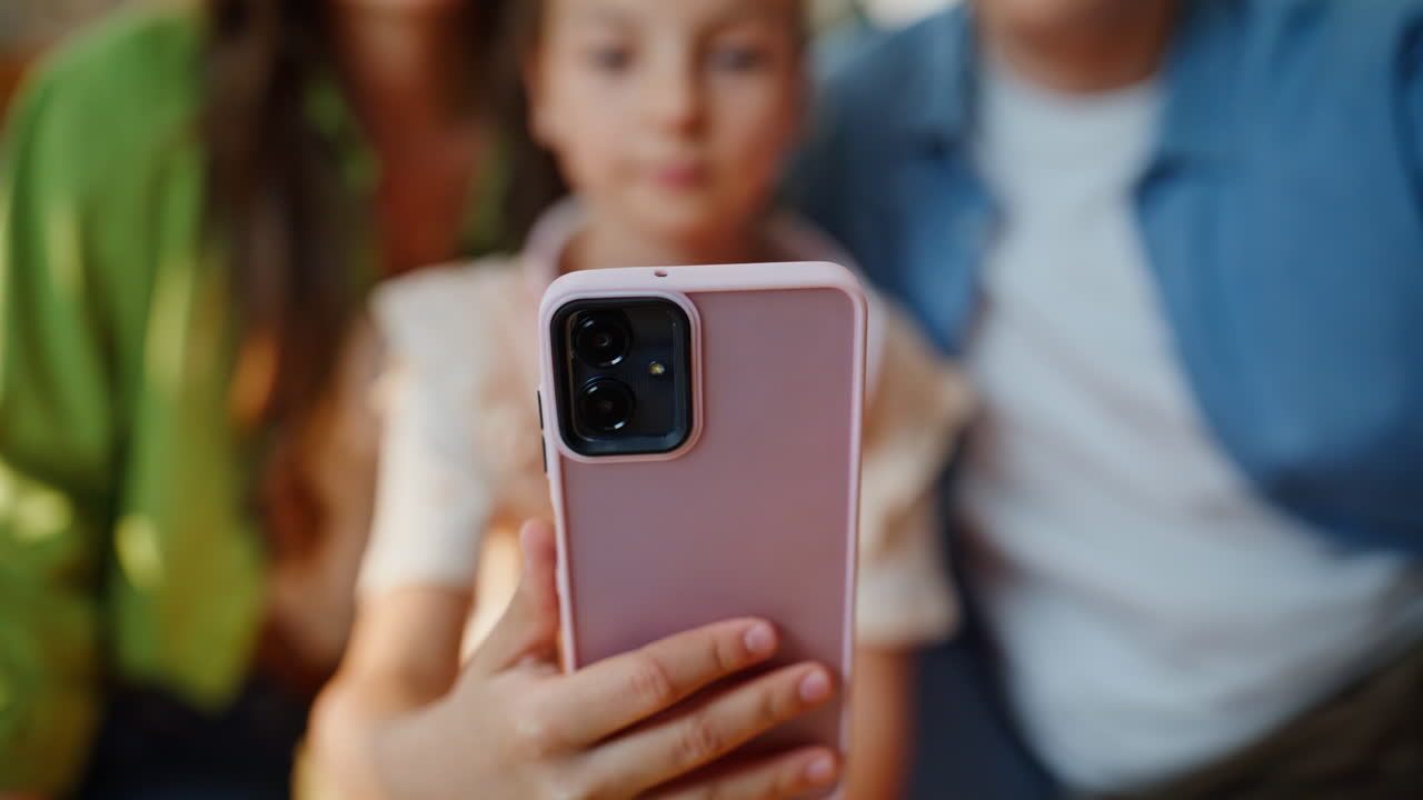 Bambini che fanno videochiamate con i genitori su smartphone e si salutano da vicino in un soggiorno soleggiato