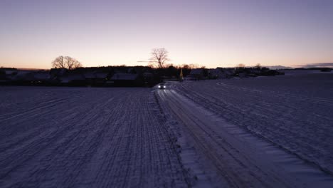 drone view of car driving on icy road in danish winter countryside - dolly shot