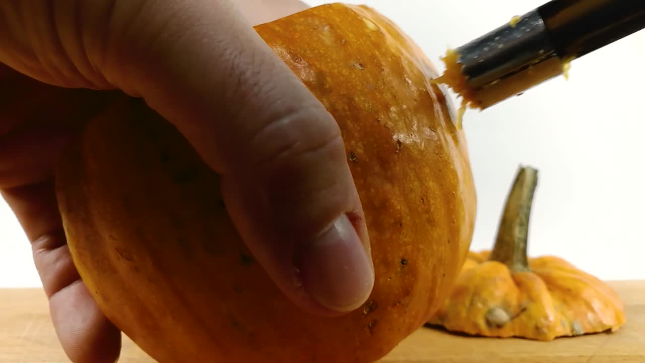 Carving pumpkin part 3, Person carving eye into Halloween pumpkin with a small  serrated apple corer knife on wooden chopping board, STILL, ISOLATED, SLOMO
