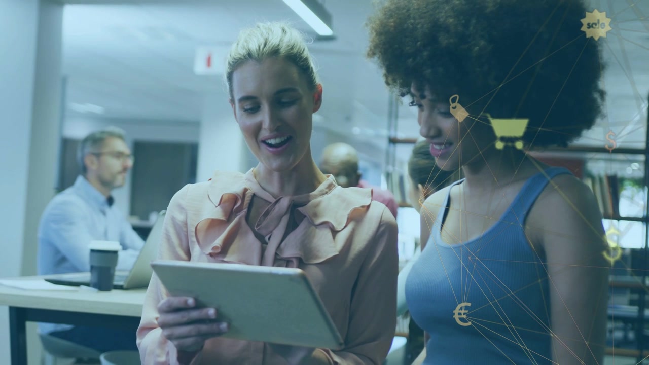 Blonde woman tapping tablet curly colleague leaning in reviewing ecommerce cart and currency icons