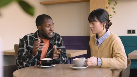 Man-And-Woman-Talking-Together-While-Sitting-At-Table-In-A-Coffee-Shop-1