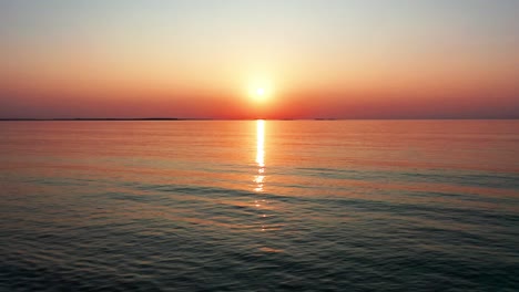 gorgeous beach sunrise with bright glowing sun casting colorful red, orange, purple and yellow reflections over peaceful rippling waves of the sea