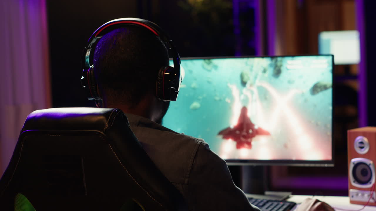 Man playing SF space videogame on PC screen in dark room
