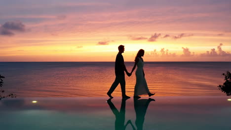 romantic couple walking by infinity pool at sunset