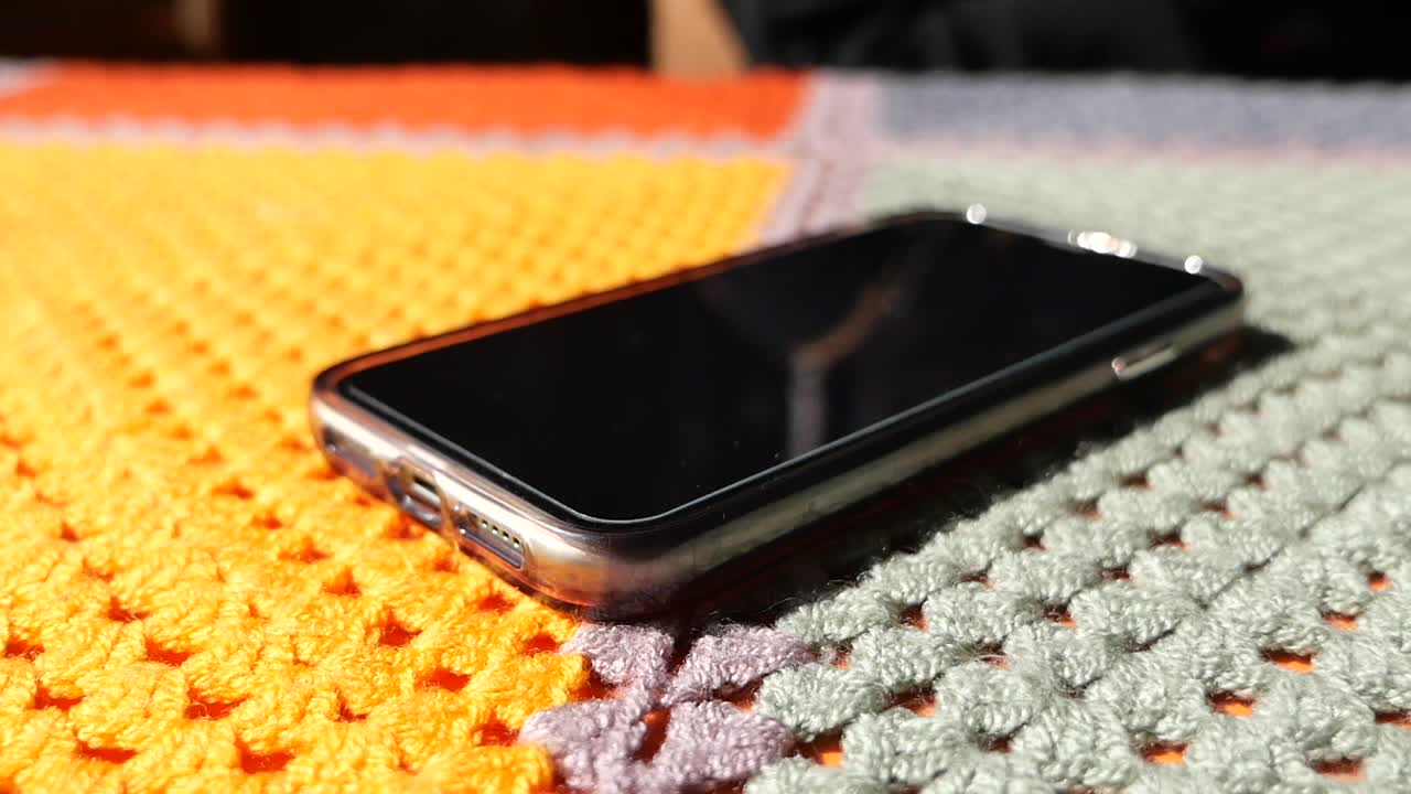 Hand holding a smartphone on a colorful crocheted blanket